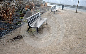 Perennial bed mulched with gray gravel in front of a limestone stone wall in a square with benches with wood paneling, beige path