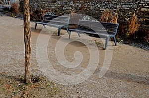 Perennial bed mulched with gray gravel in front of a limestone stone wall in a square with benches with wood paneling, beige path