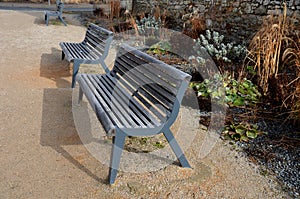 Perennial bed mulched with gray gravel in front of a limestone stone wall in a square with benches with wood paneling, beige path