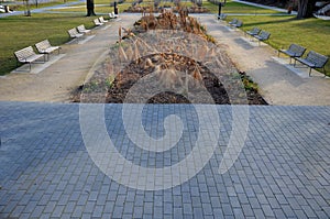Perennial bed mulched with gray gravel in front of a limestone stone wall in a square with benches with wood paneling, beige path