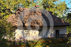 Scenic landscape view of small ancient clay house with a garden surrounded by a wicker fence in sunny autumn day