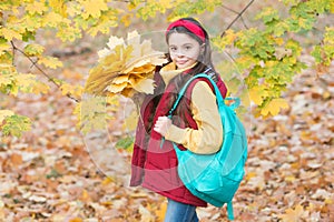 Perfect autumn day of cheerful girl with school bag and maple leaves arrangement walking in fall season park in good