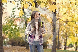 perfect autumn day of cheerful kid with school bag walking in fall season park in good weather, happy childhood