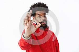 Perfect. Blurred shot of african american bearded guy in red hoodie pulling hand in focus towards camera showing okay