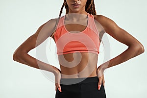 Perfect body. Cropped photo of muscular young african woman in sportswear keeping arms on hips while standing against