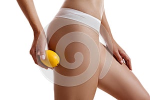 Perfect body of girl in white underwear touching her hip with lemon, isolated on white. Plastic surgery and aesthetic