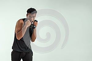 Perfect body. Muscular young african man exercising with dumbbells while standing against grey background