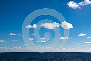 Perfect clouds in blue sky, fluffy clouds in bright sky over ocean. Dark blue calm sea water.