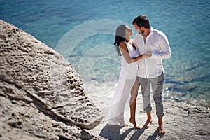 Perfect couple portrait, standing on stone beach behind mediterranean sea, honeymoon in Greece.