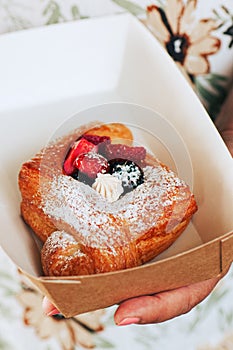 Perfect danish puff pastry with cream and berries in a craft paper box in a hand. Take away food concept