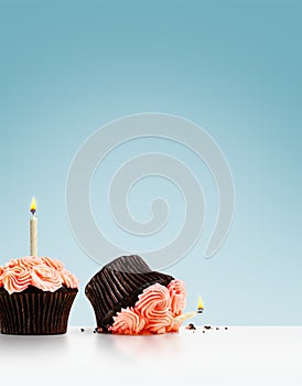 Perfect and dropped pink cupcakes with candles on blue