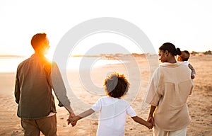 Perfect evening with family. Back view of parents walking on the beach with two kids, enjoying sunset by seaside