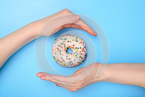 Perfect food creating concept. Photo of tasty donut with colorful sprinkles and two hands making roof catching the flying object