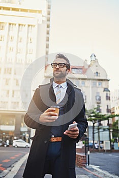 The perfect getup for a guy on the go. a stylish man with coffee and phone in hand while out in the city.