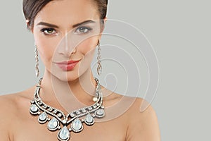 Perfect jewelry model woman with dark brown hair and shiny fresh skin wearing diamond earring and necklace posing against grey