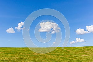 The perfect landscape of green grass field and white fluffy clouds in blue sky.