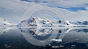 Perfect mirror reflections of snowy mountains and icebergs in Antarctica.