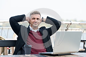 Perfect morning. Handsome smiling man enjoying his coffee. Happy hipster holding laptop and coffee cup cafe terrace