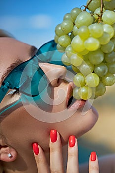 Perfect nail manicure of a woman in blue sunglasses, a summer woman eating grapes. Red professional nail manicure