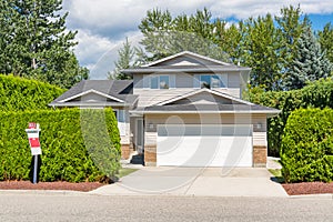 A perfect neighbourhood. Main entrance of big residential house with concrete driveway and green hedge in front. Family house for