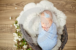Perfect newborn baby girl in blue blanket in a wicker basket decorated with branches cherry blossoms