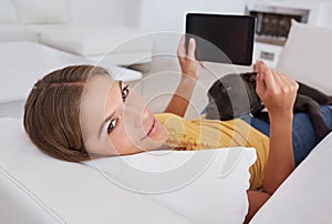 The perfect place for a bit of surfing. Portrait of a young woman using a digital tablet while lying on a sofa with her