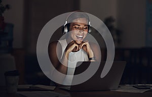 The perfect podcast to take her through the night. a young businesswoman using headphones and a laptop during a late