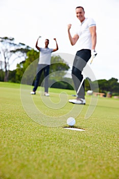The perfect putt. Low angle shot of a golf ball approaching the hole while two golfers look on.