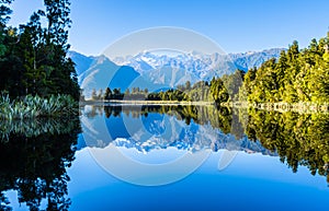 Perfect reflection in Lake Matheson surrounded by beautiful natural forest under blue sky