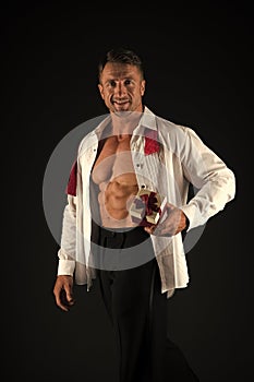 A perfect romantic gift for her. Handsome man holding gift on black background. Athletic guy with fit torso and gift box