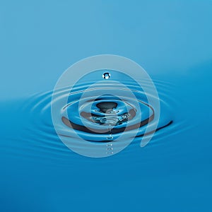 Perfect water droplet creating ripples on serene blue surface