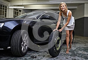 The perfect woman. A beautiful young woman changing her cars tyre in a parkade.