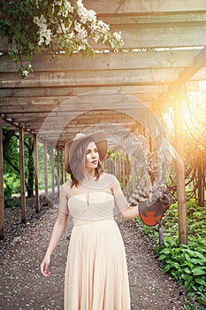 Perfect woman in fedora hat in spring garden. Girl training hawk bird outdoors