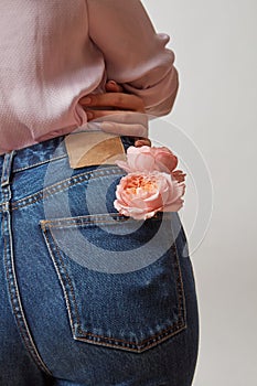 Perfect woman`s bottom in a blue jeans and fresh roses living coral color in a back pocket on a light gray background