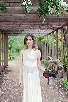 Perfect young woman fashion model in white dress with bird outdoors in park