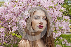 Perfect young woman with natural makeup and healthy long brown hair in blossom park outdoors. Natural female beauty portrait