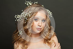 Perfect young woman with white flowers in blonde hair on dark background