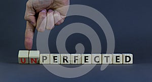 Perfected or unperfected symbol. Businessman turns wooden cubes and changes the word unperfected to perfected on a beautiful grey