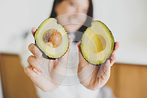 Perfectly ripe avocado halves in hands of happy woman in modern kitchen, close up. Healthy eating