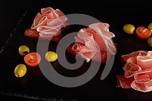 Perfectly served prosciutto or jamon with olives on a black board.