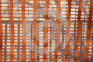 Perforated plastic orange safety net for construction site. Behind there are a grey wire netting and a white wall