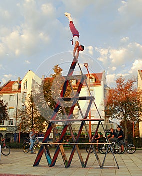 A performance artist balances on top of a house of cards