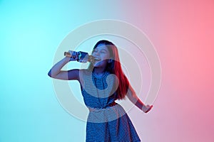 Performance. Little girl, child singing in microphone over gradient blue pink studio background in neon light. Concept