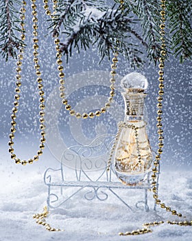 Perfume bottle on the bench in the snowy forest.Spruce branches is decorated of the gold beads.