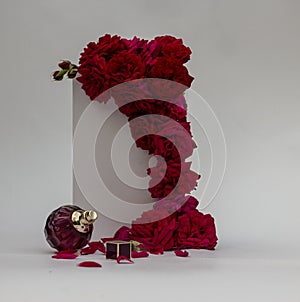 A perfume bottle with red rose flowers and pearls on a white background. Side view, flat surface.