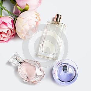 Perfume bottles with flowers on light background. Perfumery, cosmetics, fragrance collection. Flat lay