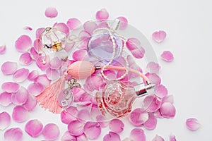 Perfume bottles with necklaces among flower petals on white background. Perfumery, cosmetics, fragrance collection