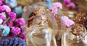 Perfume in glass bottles with cork caps among flowers on wooden background.