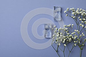 Perfume mini bottles and flowers on violet background