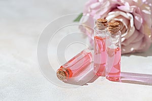 Perfumed Rose Water or essential oil in glass bottle and rose flower on a light background